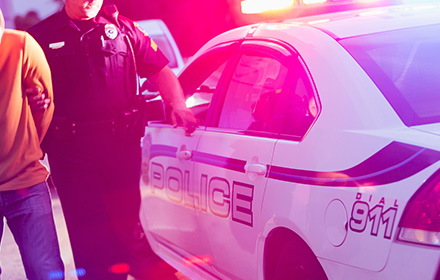 Police Officer Walking Next To Man in Handcuffs and Police Car After an Arrest