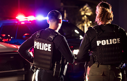 Backside of Law Enforcement Officers in a Police Vest With Vehicle Sirens in the Background