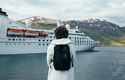 Back View of Young Traveler Wearing a Backpack While Facing a Cruise Ship