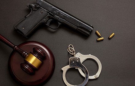 Judge Gavel, Handcuffs and Gun on Top of a Gray Surface To Represent the Consquences of Assault Charges